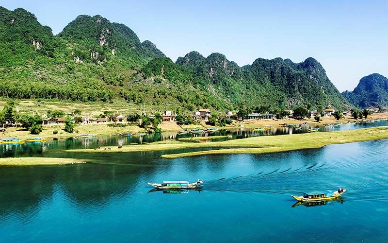 Một bãi biển vắng vẻ với cát vàng và sóng vỗ nhẹ, phía xa là núi